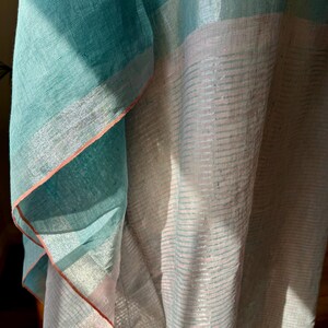 May include: A teal and pink linen fabric with a silver stripe pattern. The fabric is folded and draped, showing the texture and sheen of the material.