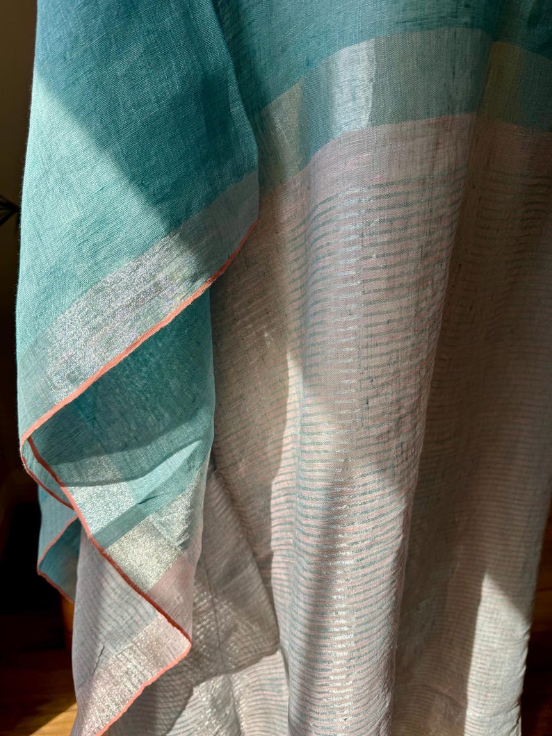 May include: A teal and pink linen fabric with a silver stripe pattern. The fabric is folded and draped, showing the texture and sheen of the material.