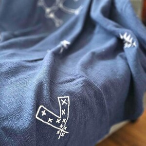 May include: A navy blue throw blanket with a white embroidered pattern of geometric shapes and arrows.