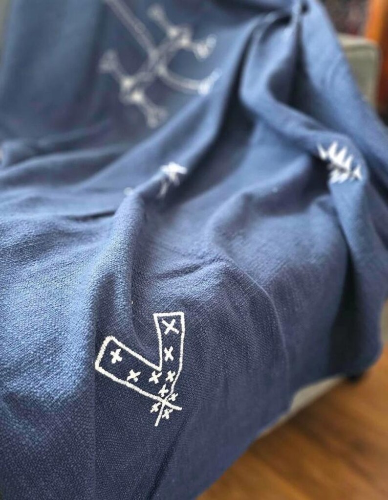 May include: A navy blue throw blanket with a white embroidered pattern of geometric shapes and arrows.