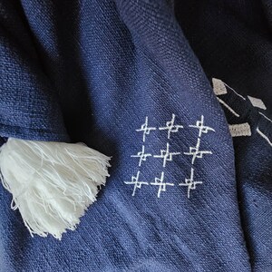 May include: A navy blue throw blanket with white fringe and a white embroidered pattern of crosses.