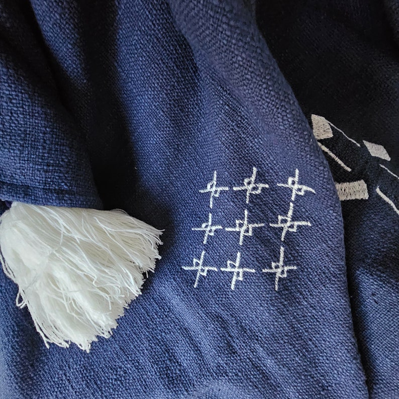 May include: A navy blue throw blanket with white fringe and a white embroidered pattern of crosses.