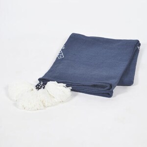 May include: A navy blue throw blanket with white embroidered geometric designs and white pom-poms.