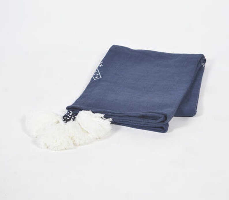 May include: A navy blue throw blanket with white embroidered geometric designs and white pom-poms.