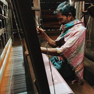 Indian artisan at work weaving linen kaftan on traditional handloom.
