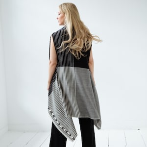 May include: A black and gray striped sleeveless vest with a geometric pattern. The vest is draped over a person's shoulders and has a long, flowing design.