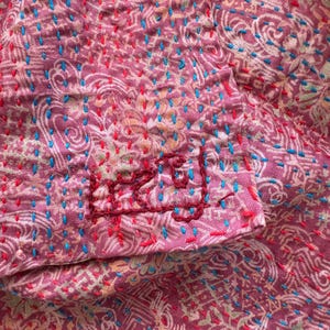 Close up detail of floral patterns on a upcycled sari silk scarf with hand embroidered Kantha running stitch to create a lightly quilted look, the scarf is handmade in India and bears the artisans signature in the Bengali language.