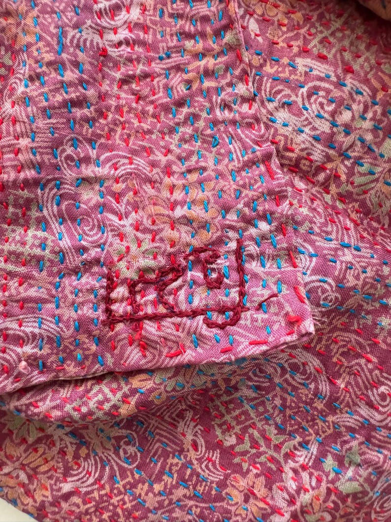 Close up detail of floral patterns on a upcycled sari silk scarf with hand embroidered Kantha running stitch to create a lightly quilted look, the scarf is handmade in India and bears the artisans signature in the Bengali language.