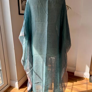 May include: A teal blue linen kaftan with a loose fit and a flowing silhouette. The kaftan has a V-neckline and a long, flowing hem.