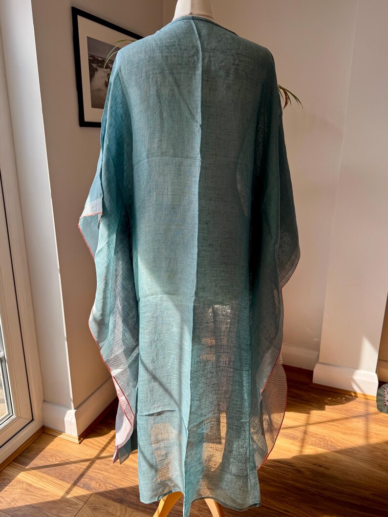 May include: A teal blue linen kaftan with a loose fit and a flowing silhouette. The kaftan has a V-neckline and a long, flowing hem.