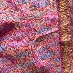 Close up detail of hand embroidery on a Kantha sari silk scarf with a decorative embellished border and abstract print in pink and light blue colours.