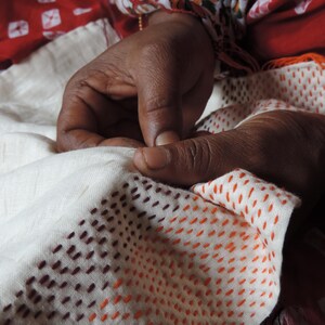Hands of Indian artisan sewing colourful tiny running stitches on vintage sari silk fabric
