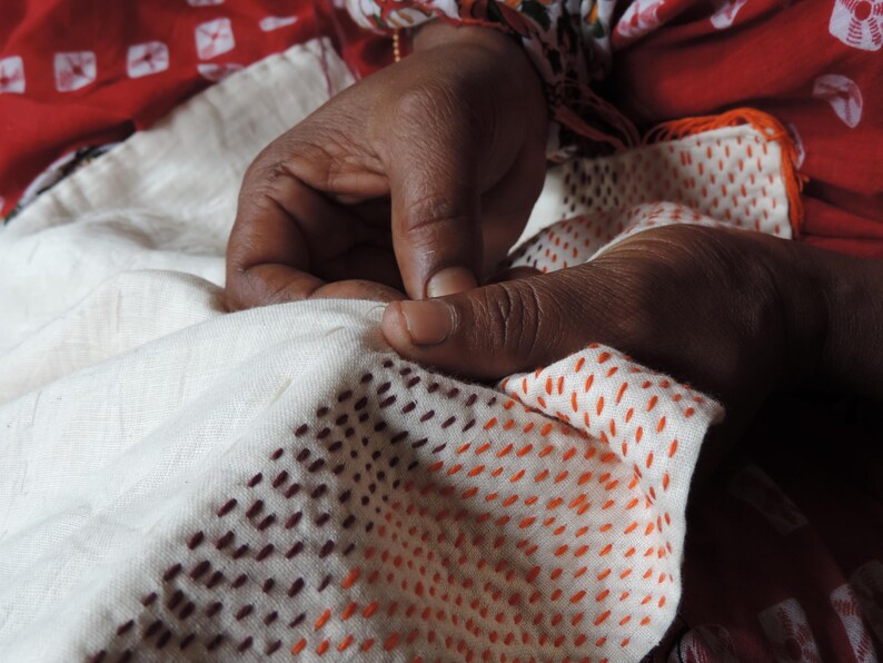 Hands of Indian artisan sewing colourful tiny running stitches on vintage sari silk fabric