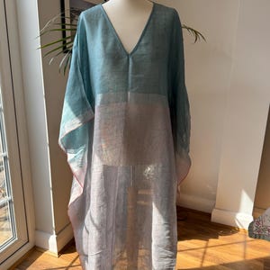 May include: A long, flowing, light blue and gray linen kaftan with a V-neckline. The kaftan has a loose, comfortable fit and is perfect for warm weather.