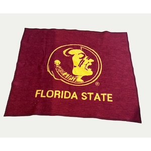 May include: A maroon blanket featuring the Florida State Seminoles logo in yellow. The logo is a stylized image of a Seminole warrior's head. The words "FLORIDA STATE" are printed in yellow below the logo.