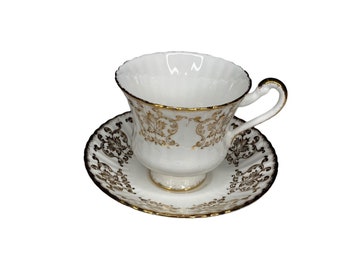 May include: A white teacup and saucer with a gold floral pattern. The cup has a fluted rim and a handle. The saucer has a scalloped edge.