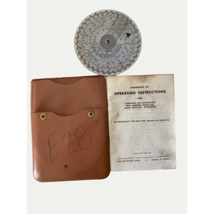 May include: A brown leather case with a metal snap closure and the text "E28" written on it. The case is open to reveal a white booklet with the title "Handbook of Operating Instructions for Computer-Air Navigation, True Airspeed, Mach No, Wind Solution, Supersonic." The booklet is manufactured by Felsenthel Instruments Company, 7413 West Wilson Avenue, Chicago 31, Illinois.