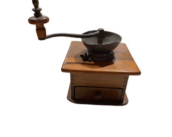 Op de afbeelding: Antiek houten koffiemolen met een metalen molen en een lade. De molen heeft een houten handvat en een metalen kruk.