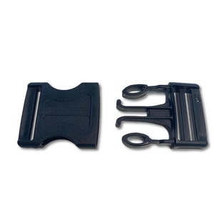 Op de afbeelding: Twee zwarte plastic gespen, een met een zijdelingse ontgrendelingsgesp en de andere met een zijdelingse ontgrendelingsgesp en een dubbele lus.