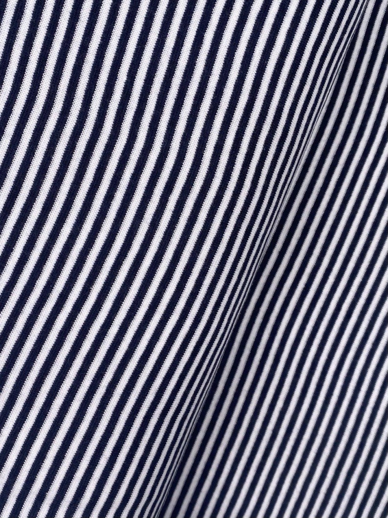 May include: Close-up of a white and navy blue striped fabric. The fabric has a diagonal pattern and a soft, textured feel.