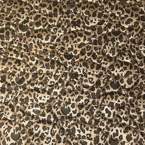 Op de afbeelding: Close-up van een gewatteerde stof met een luipaardprintpatroon. De stof heeft een herhalend ontwerp van donkerbruine vlekken op een tan achtergrond. Het quilten creëert een gestructureerd, dimensionaal effect.