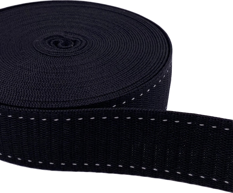 May include: Black webbing with white stitching. The webbing is rolled up and the stitching is visible on the edge.