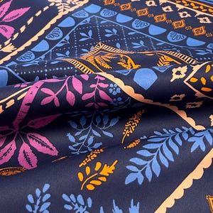 May include: Close-up of a navy blue fabric with a repeating floral pattern. The design features pink, blue, and orange botanical elements within geometric borders. The fabric has a soft, flowing appearance.