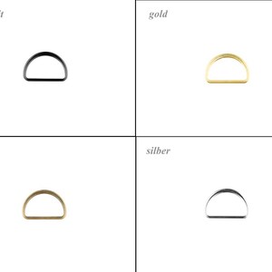 Pode incluir: Uma grade de quatro argolas em D com diferentes acabamentos. No canto superior esquerdo, a etiqueta anthrazit mostra uma argola preta. No canto superior direito, a etiqueta gold mostra uma argola dourada. No canto inferior esquerdo, a etiqueta brass mostra uma argola de latão. No canto inferior direito, a etiqueta silber mostra uma argola prateada.