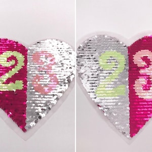 Può includere: Un cerotto di paillettes a forma di cuore con i numeri 2 e 3. Le paillettes sono reversibili, quindi puoi capovolgerle per cambiare il colore dei numeri. Un lato è rosa con numeri verdi, e l'altro lato è argento con numeri rosa.