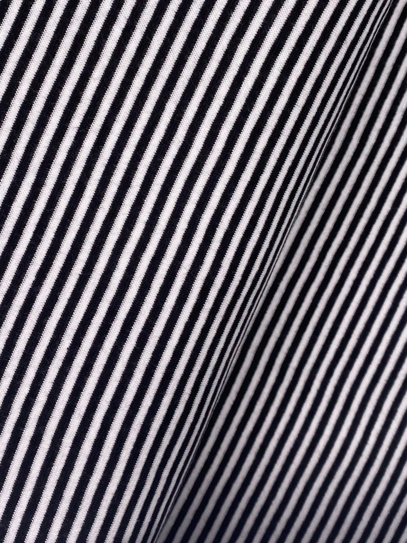 May include: Black and white striped fabric with a diagonal pattern. The fabric is folded in half, creating a crease down the center.
