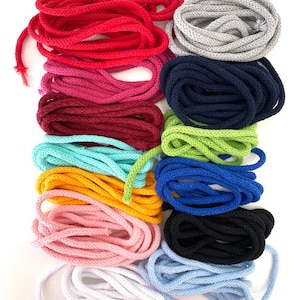 Könnte beinhalten: Eine Sammlung von 12 Spulen mit farbigem Baumwollschnur, jede zu einer ordentlichen Spule gewickelt. Die Schnüre sind in verschiedenen Farbtönen von Rot, Rosa, Blau, Grün, Gelb und Weiß.