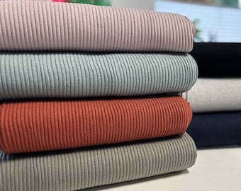 Puede incluir: Una pila de cinco muestras de tela de canalé en diferentes colores, incluyendo gris claro, gris oscuro, óxido y azul marino.