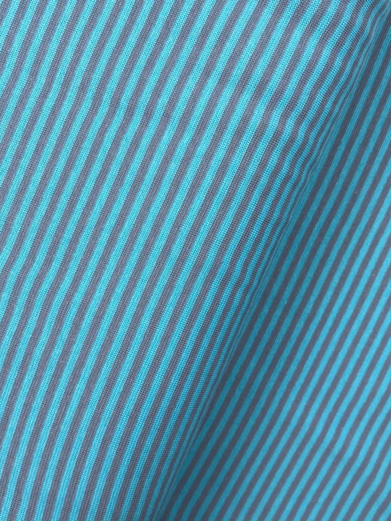 May include: Close-up of a blue and gray striped fabric. The fabric has a diagonal pattern and a soft, textured feel.