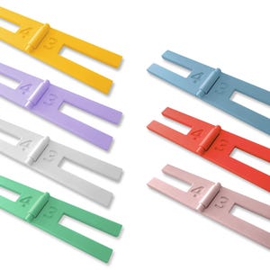 May include: Six colorful plastic spacers, each with a hinge and the numbers "4.33" printed on them. The spacers are yellow, purple, white, green, blue, and pink.