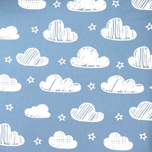 Op de afbeelding: Een naadloos patroon met witte wolken en sterren op een lichtblauwe achtergrond. De wolken zijn getekend in een eenvoudige, handgetekende stijl met lijnen en stippen.