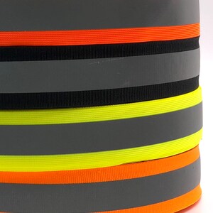 Könnte beinhalten: Vier Rollen reflektierendes Klebeband in Orange, Schwarz, Gelb und Orange. Jede Rolle hat einen silbernen reflektierenden Streifen.