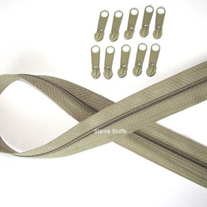 Könnte beinhalten: Ein beigefarbener Reißverschluss mit braunem Reißverschlussband und einem Satz von 10 goldenen Reißverschluss-Zügen. Der Reißverschluss ist in Form einer Acht gelegt.