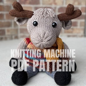 May include: Knitting machine PDF pattern for a gray knitted moose wearing a plaid scarf. The moose has brown antlers and black eyes.