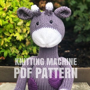 Pode incluir: Padrão PDF de máquina de tricô para um brinquedo de girafa roxo e branco. A girafa tem um rosto branco com olhos pretos e um corpo roxo com manchas roxas.