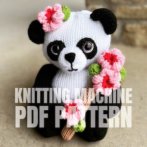 May include: Knitting machine PDF pattern for a white crocheted panda bear with black ears, eyes, and paws. The panda is wearing a pink and green flower crown and holding a brown stick with pink and green flowers.