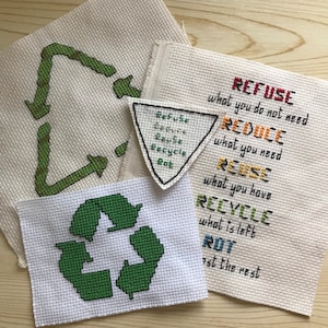 May include: Four pieces of white fabric with green and yellow cross-stitch embroidery. The fabric pieces are arranged on a wooden surface. The fabric pieces feature the words "Refuse", "Reduce", "Reuse", "Recycle", and "Rot" with the phrase "what you do not need", "what you need", "what you have", "what is left", and "ost the rest" written below each word. The fabric pieces also feature a green recycling symbol.