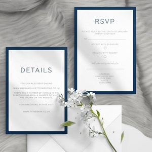 May include: Navy blue and white wedding invitation suite. The suite includes an RSVP card and a details card, both with navy blue borders and elegant typography. The RSVP card includes fields for the guest's name, acceptance, and dietary requirements. The details card provides website information.