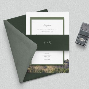 May include: A green envelope with a white card inside. The card has a green border and the text "Response" in a handwritten font. The text "Please reply by the tenth of July twenty twenty two" is below the word "Response". The text "L+B" is in a handwritten font on a green band below the text. The text "ADDRESS" is followed by an address. The card has a photo of a forest with a mountain in the background.