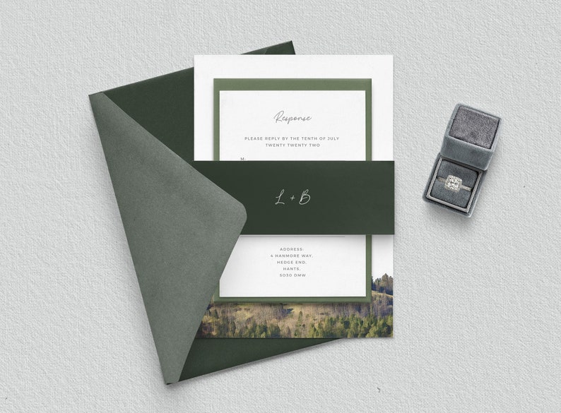 May include: A green envelope with a white card inside. The card has a green border and the text "Response" in a handwritten font. The text "Please reply by the tenth of July twenty twenty two" is below the word "Response". The text "L+B" is in a handwritten font on a green band below the text. The text "ADDRESS" is followed by an address. The card has a photo of a forest with a mountain in the background.