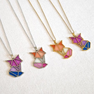 Può includere: Quattro collane con ciondoli a forma di volpe. Due hanno catene d'argento e due d'oro. I ciondoli a forma di volpe sono geometrici, con sezioni arancioni, rosa, viola, bianche e blu. I ciondoli sono alti circa 2.5 cm.