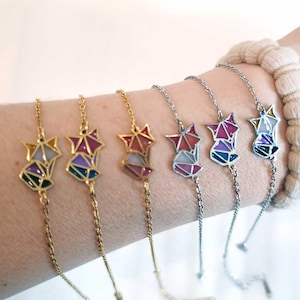 Könnte beinhalten: Fünf goldene und silberne Kettenarmbänder mit bunten geometrischen Fuchs-Anhängern. Die Anhänger sind aus Metall und haben eine Buntglasoptik.