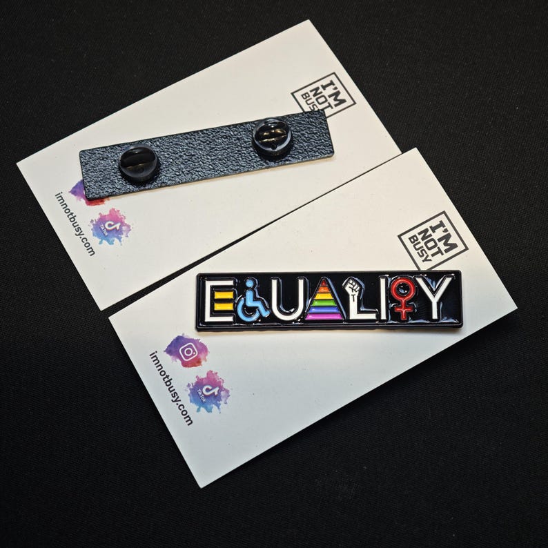 Puede incluir: Un pin rectangular de esmalte negro con la palabra EQUALITY en letras blancas. La letra Q se sustituye por un s&iacute;mbolo de silla de ruedas azul, la A por un tri&aacute;ngulo arco&iacute;ris, la L por un pu&ntilde;o en alto y la O por un s&iacute;mbolo femenino rojo.
