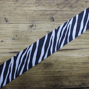 May include: Black and white zebra print ribbon. The ribbon is on a wooden surface.