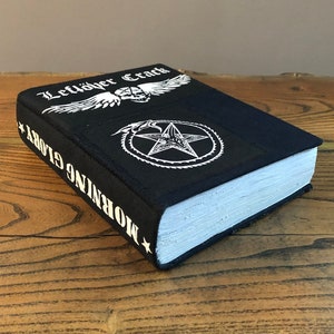 May include: A black book with the title "Morning Glory" and the text "Leftöver Crack" on the cover. The cover also features a pentagram with a snake wrapped around it and a winged skull.
