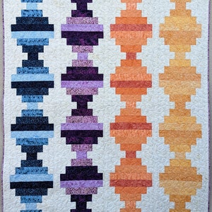 Könnte beinhalten: Eine Quiltdecke mit drei vertikalen Reihen aus bunten Quadraten. Die Quadrate sind in einem Muster angeordnet, das an einen Maschendrahtzaun erinnert. Die Quiltdecke ist aus verschiedenen Stoffen gefertigt, darunter Blau, Lila, Orange und Gelb. Die Quiltdecke ist mit einem weißen Stoff gefüttert und hat ein gestepptes Design. Die Quiltdecke trägt den Titel "Powered by Quilting".